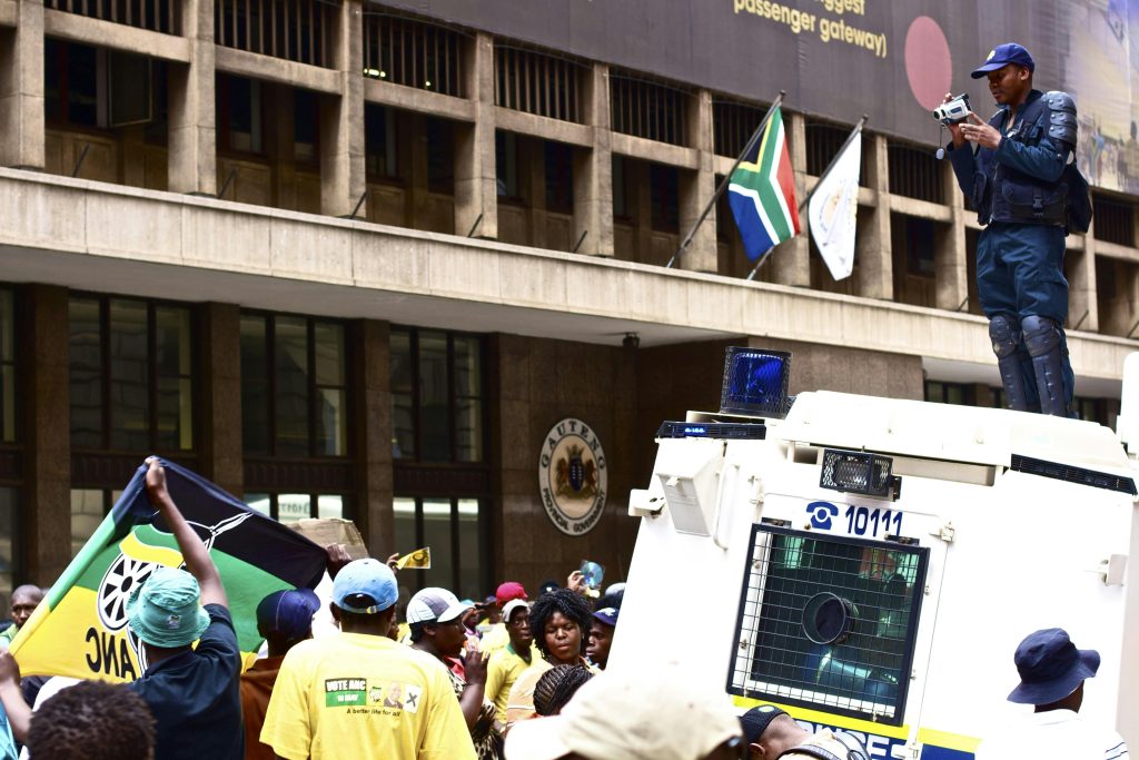 A protest with a police officer photographing the crowd in urban South Africa.