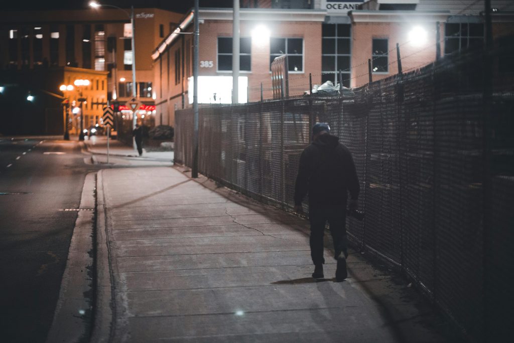 A person walks alone on a dimly lit city street at night, showcasing urban solitude.