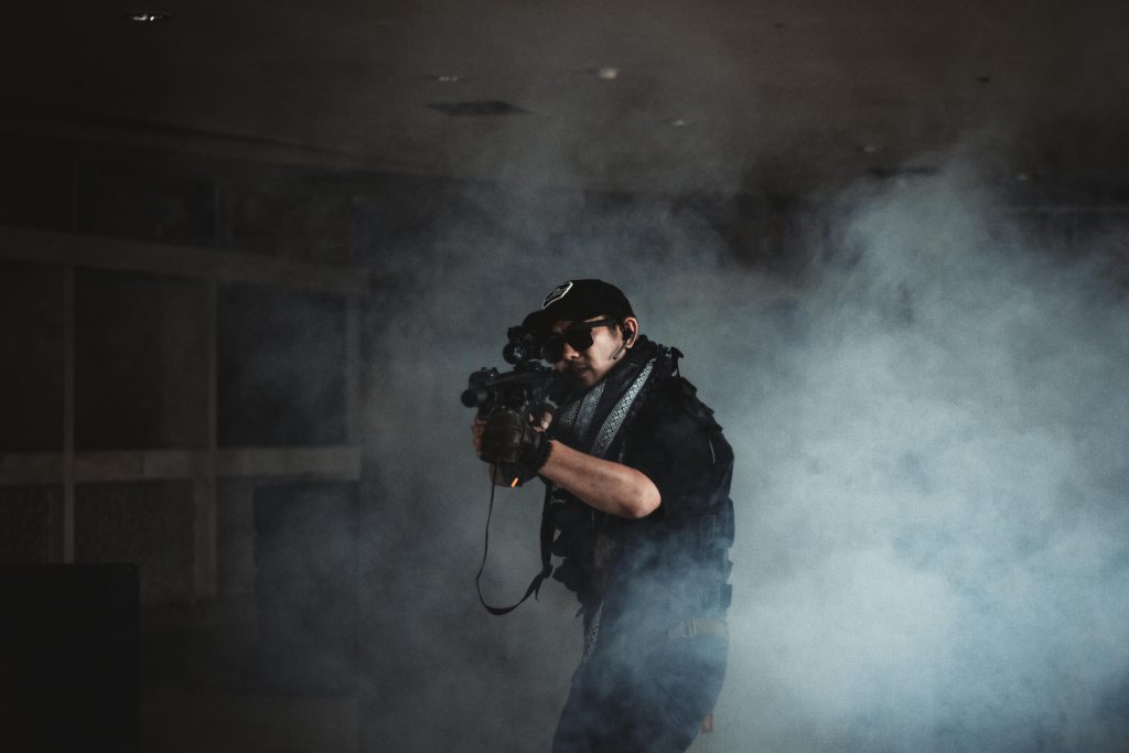 A soldier holding a rifle amidst smoke in an indoor setting, ready for action.